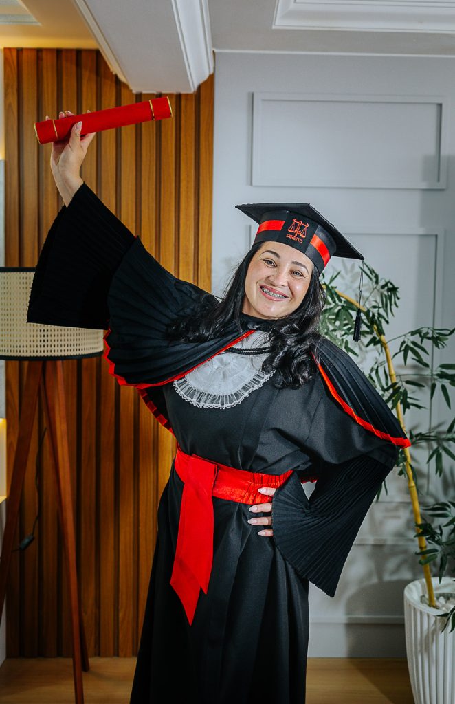 Foto de formanda de Direito em Curitiba usando beca preta e faixa vermelha em estúdio.