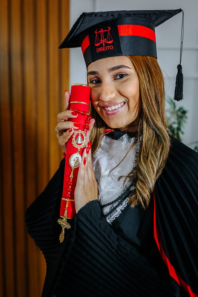 Formanda de Direito posando com beca e terço católico com fundo neutro de estúdio.